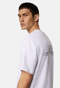 Vit bomull t-shirt med kort ärm, med ett geometriskt svart tryck på baksidan och en klassisk rund halsdesign.