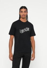 T-shirt nera con un design grafico e il testo "JACK & JONES" in bianco. Maniche corte e scollo rotondo, realizzata in tessuto morbido.