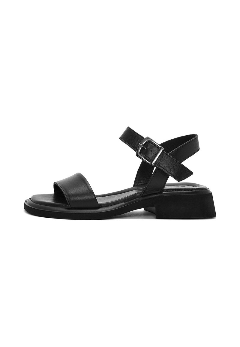 Sandaña de cuero negro con punta abierta, correa ajustable en el tobillo y tacón bajo. Textura suave con un diseño minimalista.