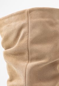 Botín de ante beige con una textura suave, que presenta un diseño arrugado y costuras visibles a lo largo de la altura.