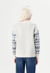 Helles graues Strickpullover mit gemusterten navyblauen Ärmeln, die geometrische Designs zeigen. Bündchen und Saum im Rippenmuster, lässige Passform.