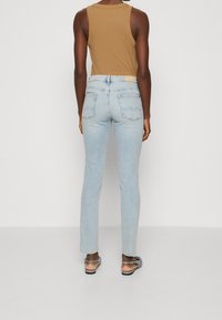 Jeans de color azul claro con un corte ajustado y bolsillos traseros, combinados con una blusa sin mangas de color topo. Los jeans cuentan con una cintura de altura media y un diseño minimalista.