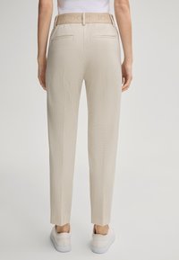 Beige Hosen mit Karomuster, hoher Taille und glatter Textur. Mit einer versteckten Gesäßtasche und einem markierten Taillenbund.