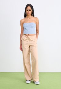 Beige wide-leg pants with elastic waistband and side pockets, paired with a light blue strapless top and white sneakers.