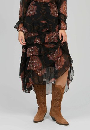 Robe noire, transparente, à imprimé floral avec des volants superposés ; bottes de cowboy en suède marron avec des broderies ornées.
