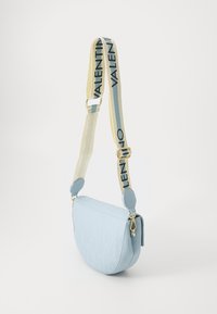 Sac à épaule en cuir bleu clair avec logo embossé, de forme semi-circulaire, bandoulière réglable avec une accent beige et un texte noir en gras.