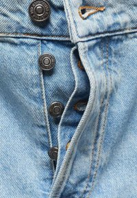 Giacca di jeans blu chiaro con una fila di cinque bottoni metallici con marchio, cuciture arancioni in contrasto e un orlo leggermente sfilacciato.