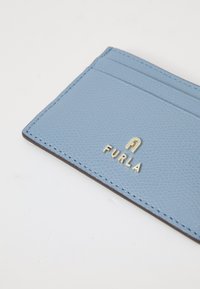 Lyseblå teksturert lær kortholder med tre kortspor og gull Furla-logo på hvit bakgrunn.