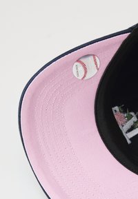 Baseball cap with a navy brim and a pink underside, featuring a baseball-themed sticker attached to its interior.