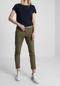 Marinblå kortärmad t-shirt med texturerad överdel, olivgröna tapered byxor och vita sneakers med svarta accenter, i kombination med ett mönstrat bälte.