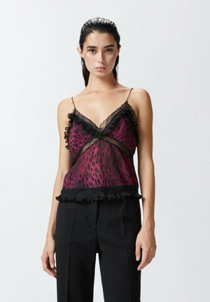 Camisón de satén en malva con un patrón de manchas, borde de encaje negro y acentos con volantes. Combinado con pantalones de vestir negros.