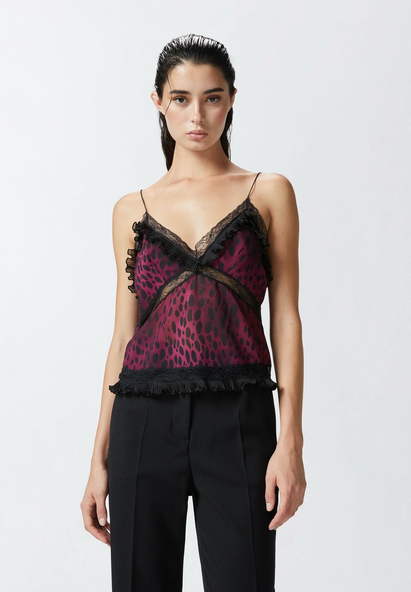 Satinasti top u boji mauve s točkastim uzorkom, crnim čipkastim detaljima i naboranim naglascima. Uparen s crnim krojenim hlačama.