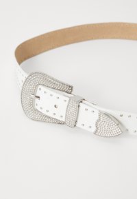 Biely kožený opasok s veľkou striebornou sponou posiatou rhinestones a srdcovými akcentmi. Obsahuje viacero dierok na nastavenie.