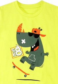Lys gul t-shirt med et tegneserie-næsehorn i en skateboarding-position. Designet inkluderer solbriller, en caps og legende grafikker.