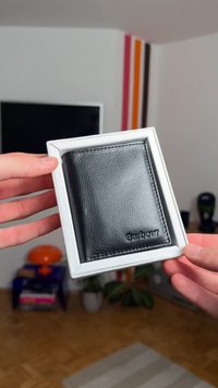 Czarny skórzany portfel w białym pudełku. Teksturowana powierzchnia z wytłoczonym logo "Barbour". Składany design na karty i gotówkę.