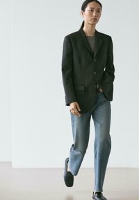 Zwart op maat gemaakt blazer met twee knopen, gestreept topje, blauwe rechte jeans en zwarte instapschoenen, die een strakke, moderne uitstraling laten zien.