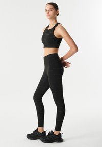 Černý sportovní set zahrnující zkrácený top se zipem a legíny s vysokým pasem. Tkanina má jemné textové vzory.