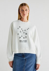 Felpa bianca con testo nero e design grafico sulla parte frontale. Presenta un collo rotondo e polsini a coste. Abbinata a una gonna di jeans.