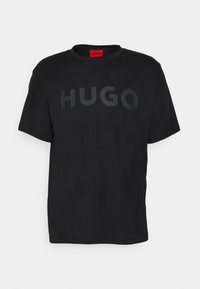 Camiseta de manga corta negra con cuello redondo. Presenta una gran impresión en textura negra de "HUGO" en la parte delantera. Está hecha de un suave tejido de algodón.