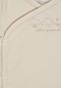 Beige baby onesie with snap buttons, featuring simple animal faces—dog, sheep, cat—and "little friends" text in light brown.