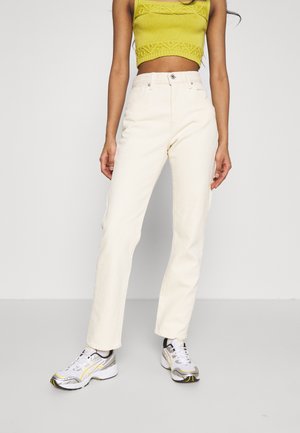 Pantalons en velours côtelé crème à rayures verticales, taille haute et jambes droites, associés à un top en tricot vert court et des baskets blanches.