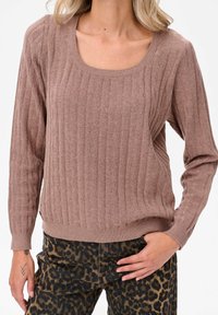 Lichtbruine geribbelde sweater met een vierkante halslijn en lange mouwen, gecombineerd met geblokte broek in luipaardprint. Zachte textuur, casual pasvorm.