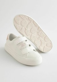 Baskets blanches avec trois bandes auto-agrippantes, un dessus en cuir lisse, une semelle en caoutchouc texturée et un accent rose sur le talon. La semelle présente un motif amusant.