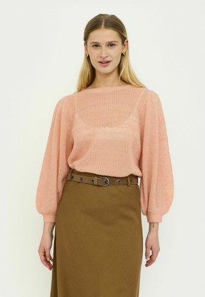 Jasnoróżowy oversize'owy sweter z grubym splotem, z długimi, bufkowatymi rękawami, zestawiony z brązową spódnicą przewiązaną paskiem. Miękka faktura, prosty design i okrągły dekolt.