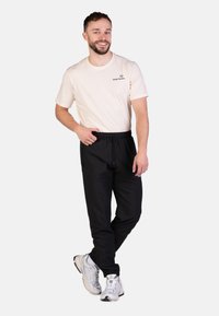 Zwarte joggings met een elastische tailleband en trekkoord, gecombineerd met een lichtbeige t-shirt met een klein logo op de borst.