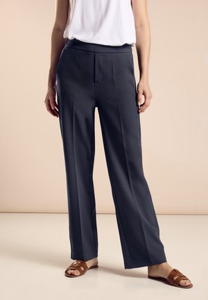 Brede broek in donkergrijze stof met een gladde textuur. Heeft een platte voorkant en verticale naden. Gecombineerd met bruine sandalen.