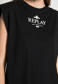 Czarna bawełniana koszulka z krótkim rękawem, z białym nadrukiem "REPLAY NOT ORDINARY" oraz logo na piersi. Gładka tekstura.