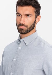 Camisa de botón azul claro hecha de tela suave, con cuello, un bolsillo en el pecho y botones blancos, con un acabado ligeramente texturizado.