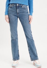 Light blue denim flared jeans with a high waist, five-pocket design, and a subtle fade. Paired with pastel sneakers for contrast.