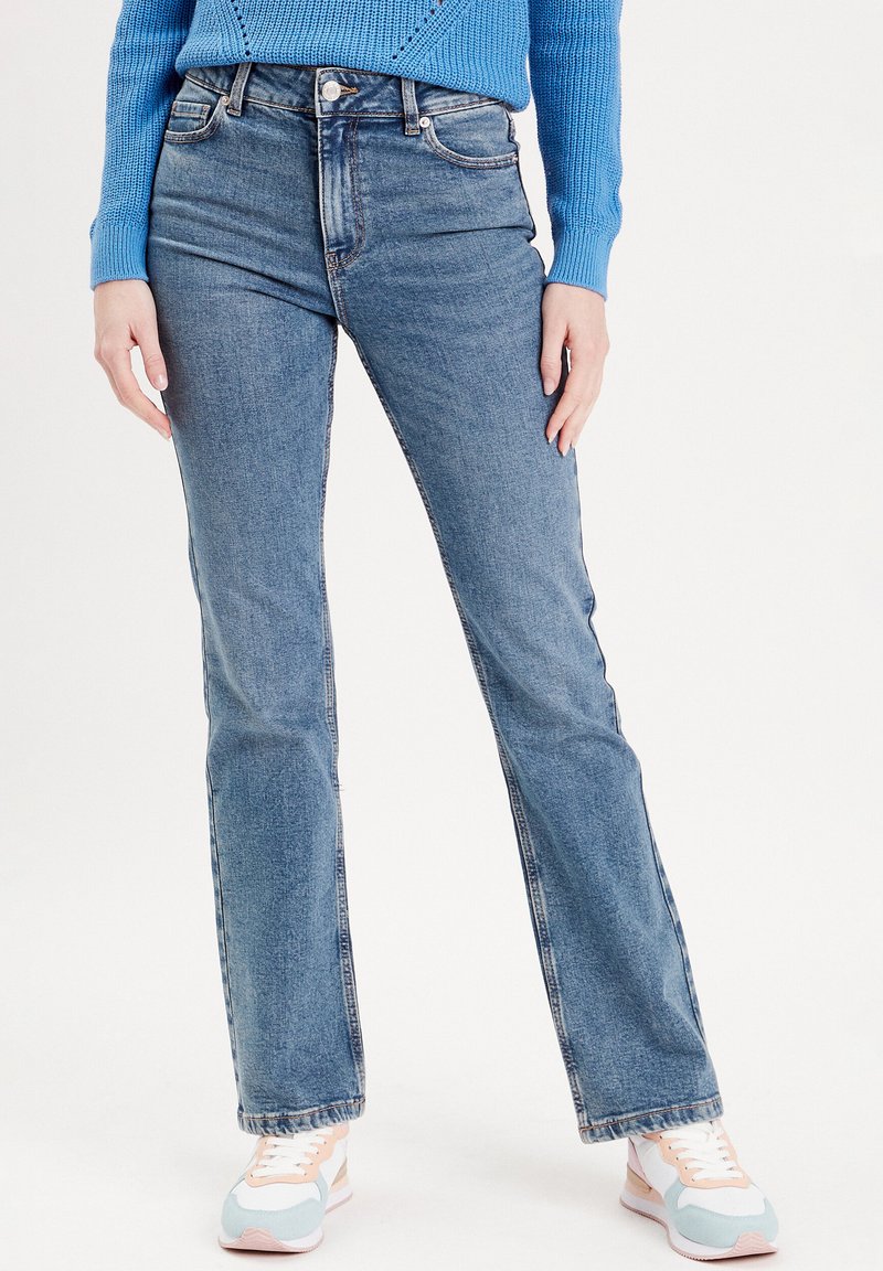 Light blue denim flared jeans with a high waist, five-pocket design, and a subtle fade. Paired with pastel sneakers for contrast.