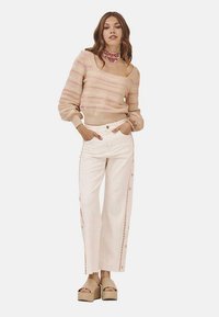 Suéter de punto con rayas rosas y beige, combinado con pantalones de pierna ancha en color crema que cuentan con botones laterales y costuras decorativas. Llevado con sandalias de plataforma.
