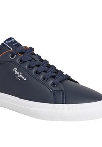 Tengerészkék színű, szintetikus bőrből készült sportcipők, lekerekített orral, fehér gumitalppal és kontrasztos barna részletekkel a nyelvén.