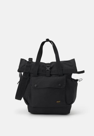 Zwarte stoffen draagtas met een bovenklep, afneembare schouderriem, voorvak met drukknopen en ritssluiting. Gladde textuur en minimalistisch ontwerp.