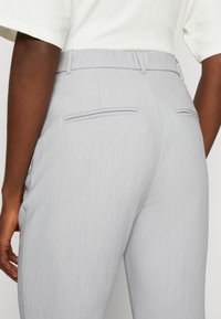 Světle šedé kalhoty vyrobené z texturované tkaniny, s přiléhavým pasem, dvěma zadními kapsami s jemnými švy a čistým designem.