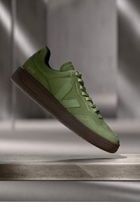 Zelena antilop tenisica s tamnim gumiranim potplatom, koja ima perforirani dio za prste, kontrastni bočni logo i ravne vezice.