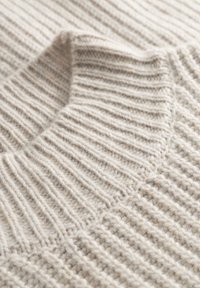 Beige gebreide trui details met een geribbelde textuur, kraagrand en zacht wolmateriaal met een chunky, gelaagd ontwerp.