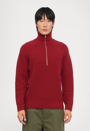 Red knit sweater with a high collar and half-zip closure. Features a textured pattern and ribbed cuffs and hem. Worn with olive green pants.
