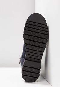 Námořnické semišové boty s podešví z texturované černé gumy, která má vzorovaný dezén a vyražené logo "TOMMY JEANS" blízko paty.