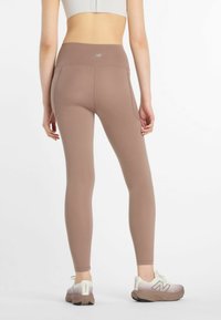 Braune Leggings mit hoher Taille aus dehnbarem Material, mit einer glatten Oberfläche und einem Logo-Akzent am Bund. Kombiniert mit hellen Sneakern.