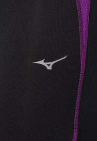 Leggings sportivi neri in tessuto strutturato, con accenti laterali viola e un piccolo logo argentato sul davanti.
