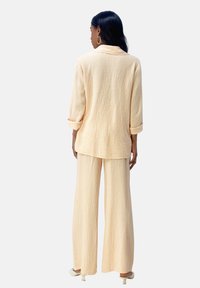 Licht perzik kleurig tweedelig outfit met een textuur, loszittend shirt met opgerolde mouwen en een wijde broek. Zacht materiaal met een ontspannen drape.