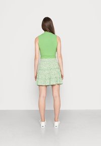 Vihreä ribattua ilman hihoja oleva paita yhdistettynä lyhyeen, vihreään kukalliseen volangihameeseen. Valkoiset kengät viimeistelevät asun. Yksinkertainen ja rento muotoilu.