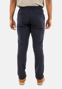 Pantalones azul marino de tela suave, con bolsillos traseros, cintura elástica y piernas ajustadas, llevados con zapatos beige.