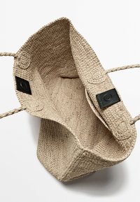 Beige geweven strooien tas met gevlochten handvatten, voorzien van zwarte leren accenten en een gestructureerde binnenkant. Open ontwerp voor gemakkelijke toegang.