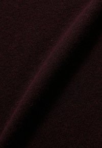 Dunkelburgunderfarbener Stoff mit weicher, strukturierter Oberfläche, zeichnet sich durch einen glatten Fall und leichtes Glänzen aus. Das Material wirkt warm und dicht.