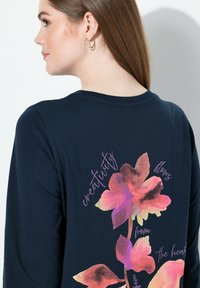 Marineblaues langärmeliges T-Shirt mit floralem Design in Rosa- und Lilatönen und dem Text "Kreativität fließt aus dem Herzen." Weiches Baumwollmaterial.